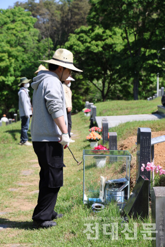 ‘오월 맞이 망월동 민족민주열사 묘역 대청소’에 참여한 자원봉사자가 잡초를 캐다 묘역의 설명을 읽고 있다.