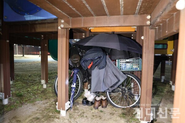 한 어린이공원에 있는 노숙인의 생활 흔적이다. 그는 놀이기구 아래 공간에 자신의 짐을 두고 생활한다. 자전거를 옷걸이 삼아 비닐봉지와 옷가지 가방이 수북이 쌓여있는 모습이다.